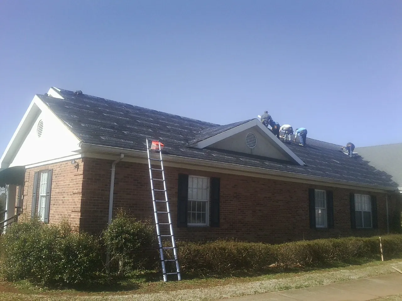 Crew tearing shingles off a brick ranch roof with a ladder set — Emergency Roof Repair work by our crew in Teachey