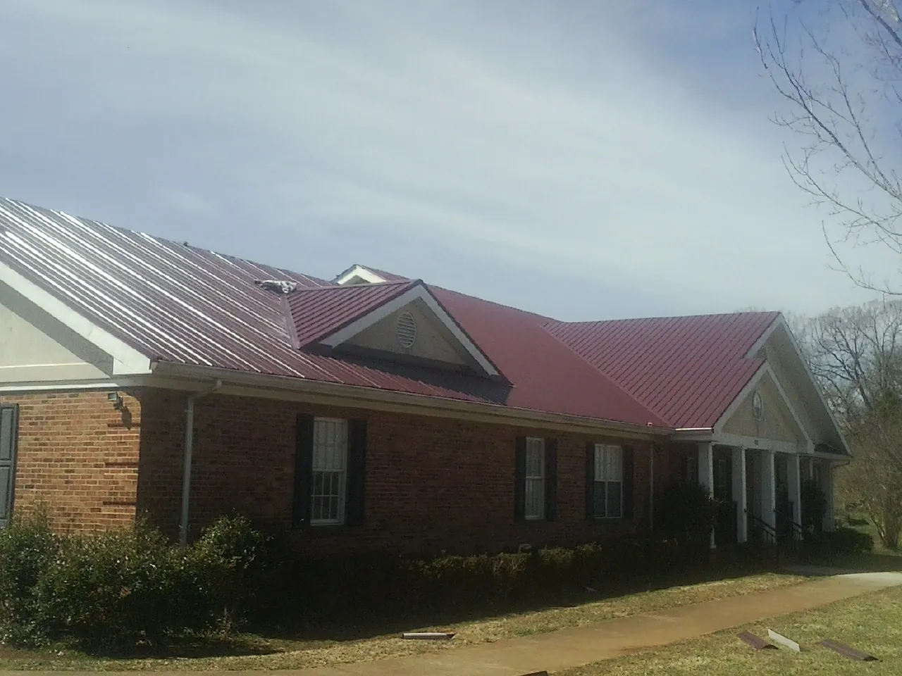 Red metal roof with gabled entries on a long brick building, from a Hail Damage Roof Repair job in Teachey