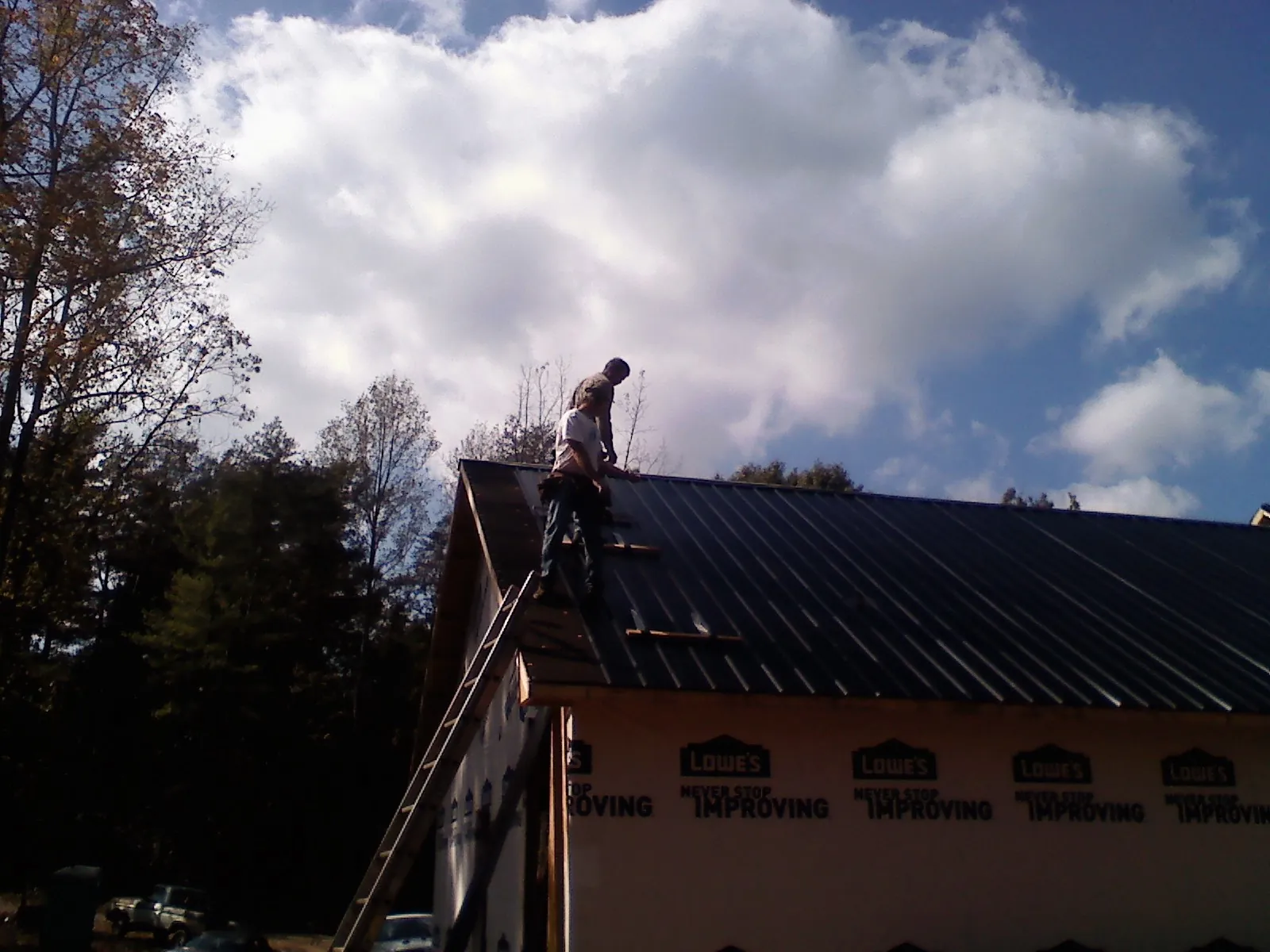 Roofer fastening dark metal panels high against a cloudy sky, from a Roof Inspection job in Teachey