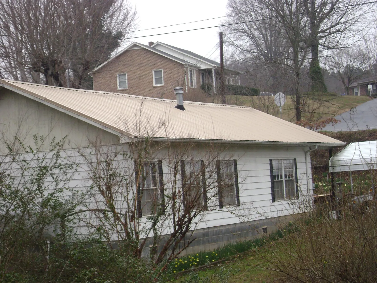 Tan metal roof on a white sided house set into a hillside — Commercial Roofing by Roofing Brothers in Teachey