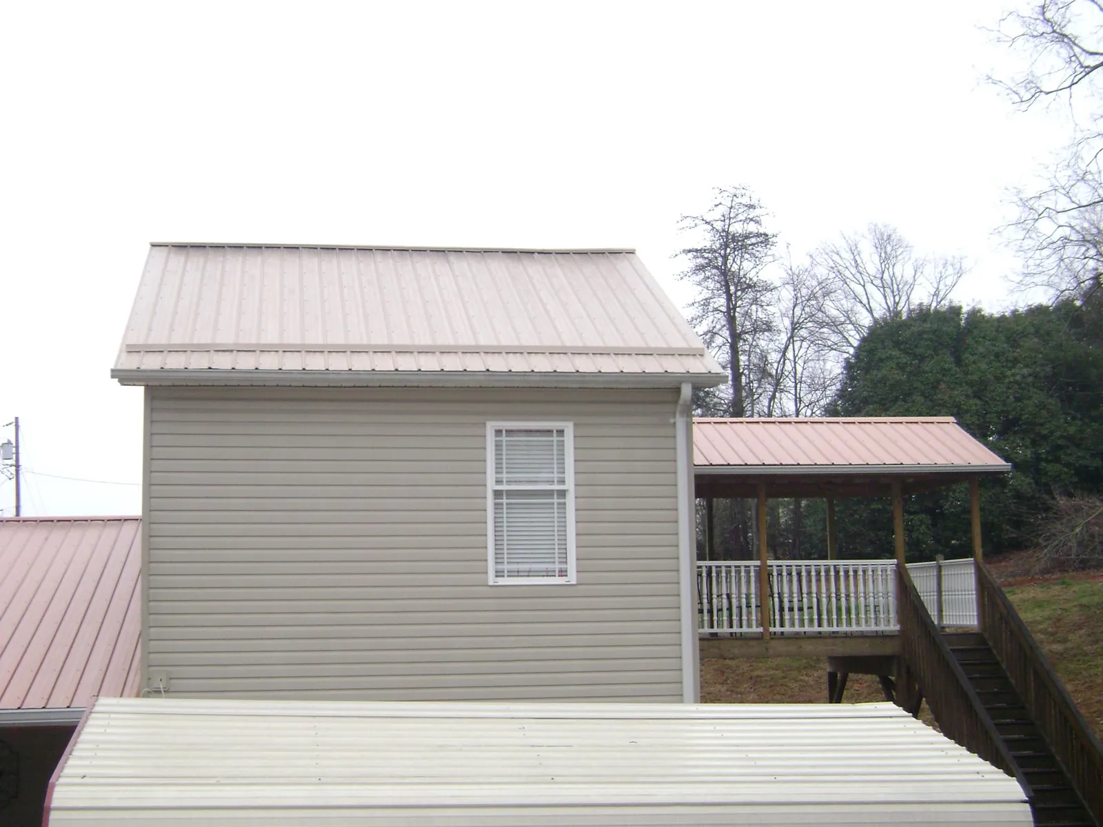 Tan metal roofs on a two story addition and attached porch, from a Roof Replacement job in Teachey